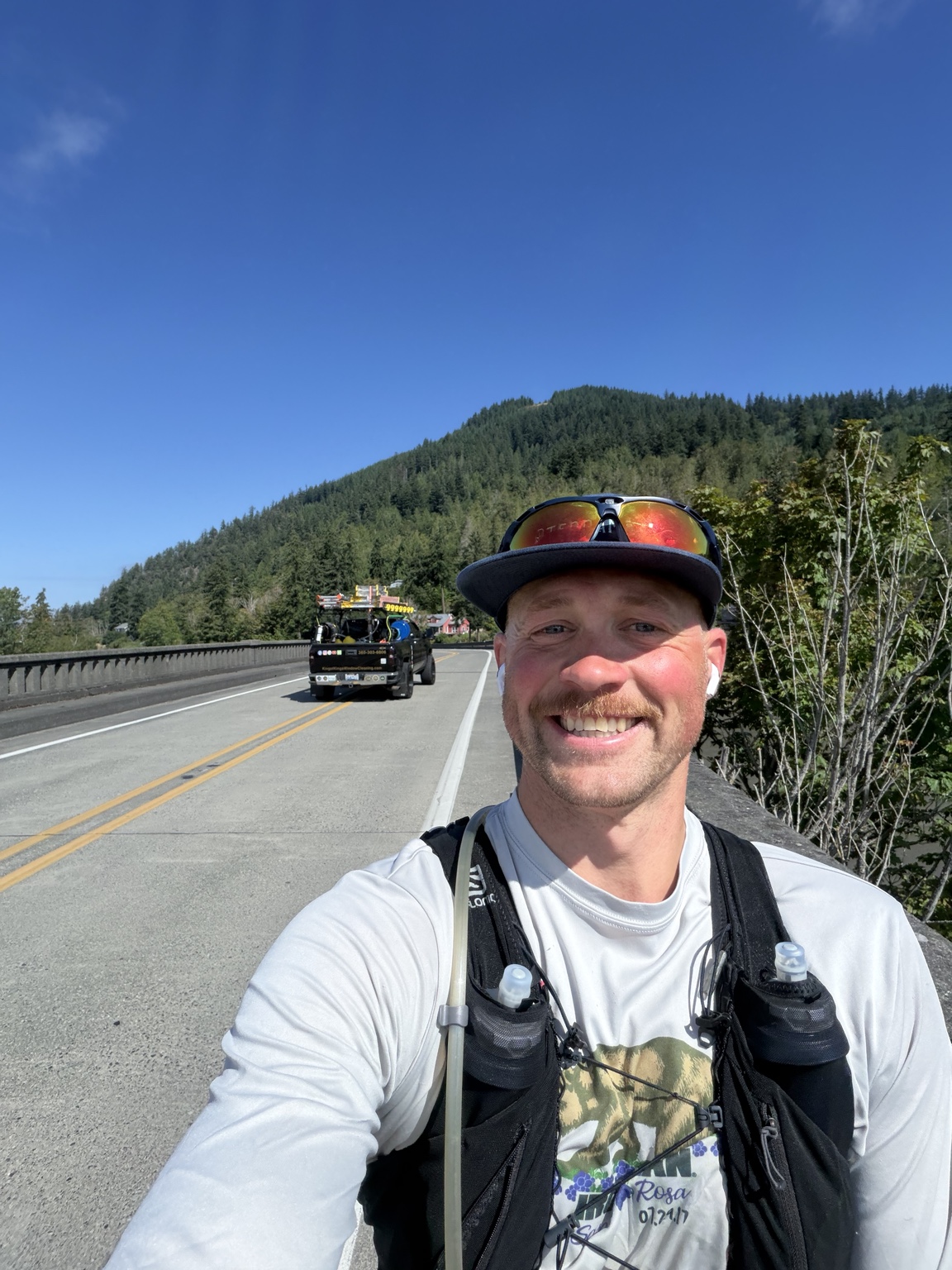 Matthew smiling on a bridge with forested hills behind him