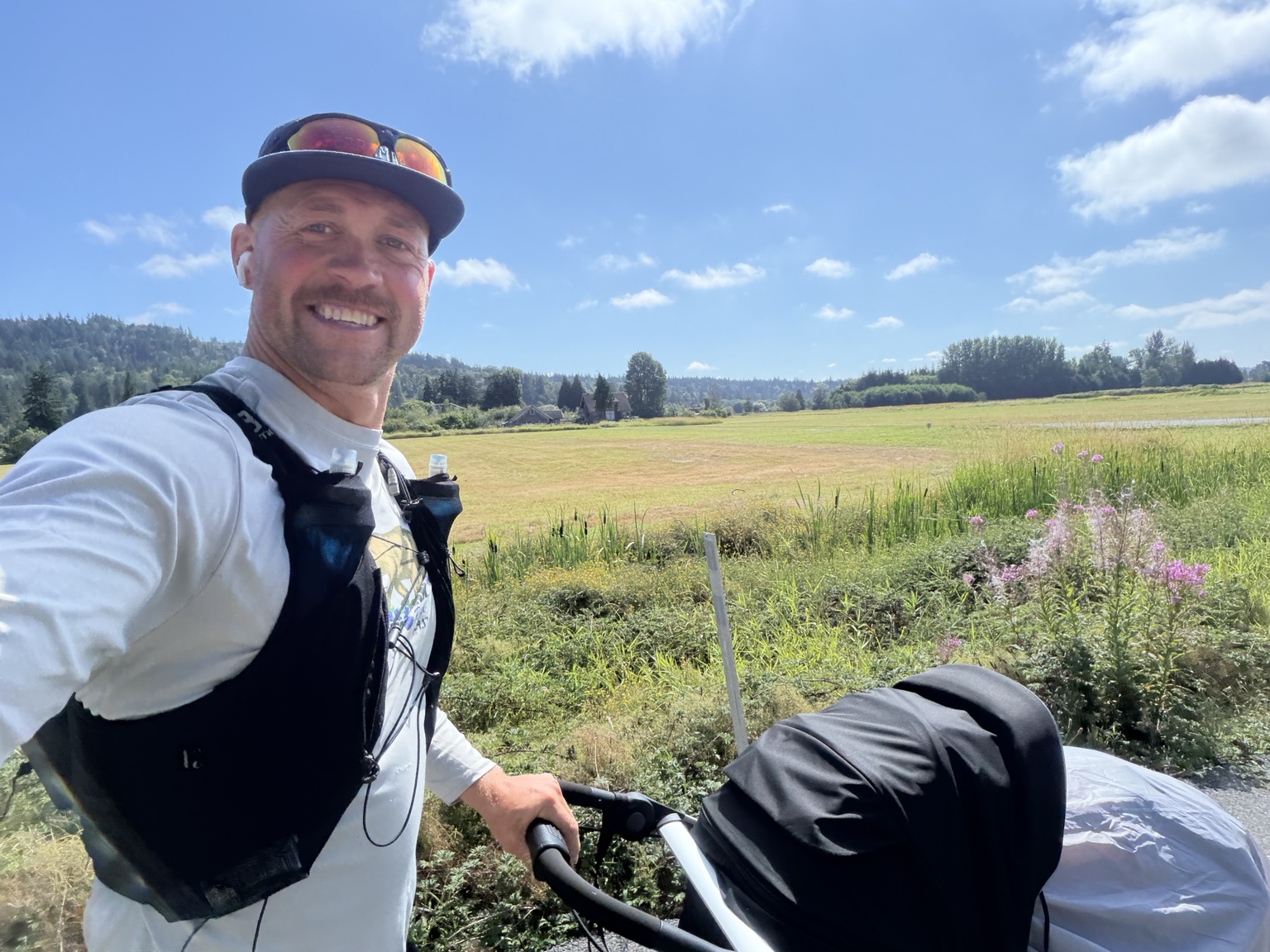 Matthew pushing his running cart past open farmland under a bright blue sky