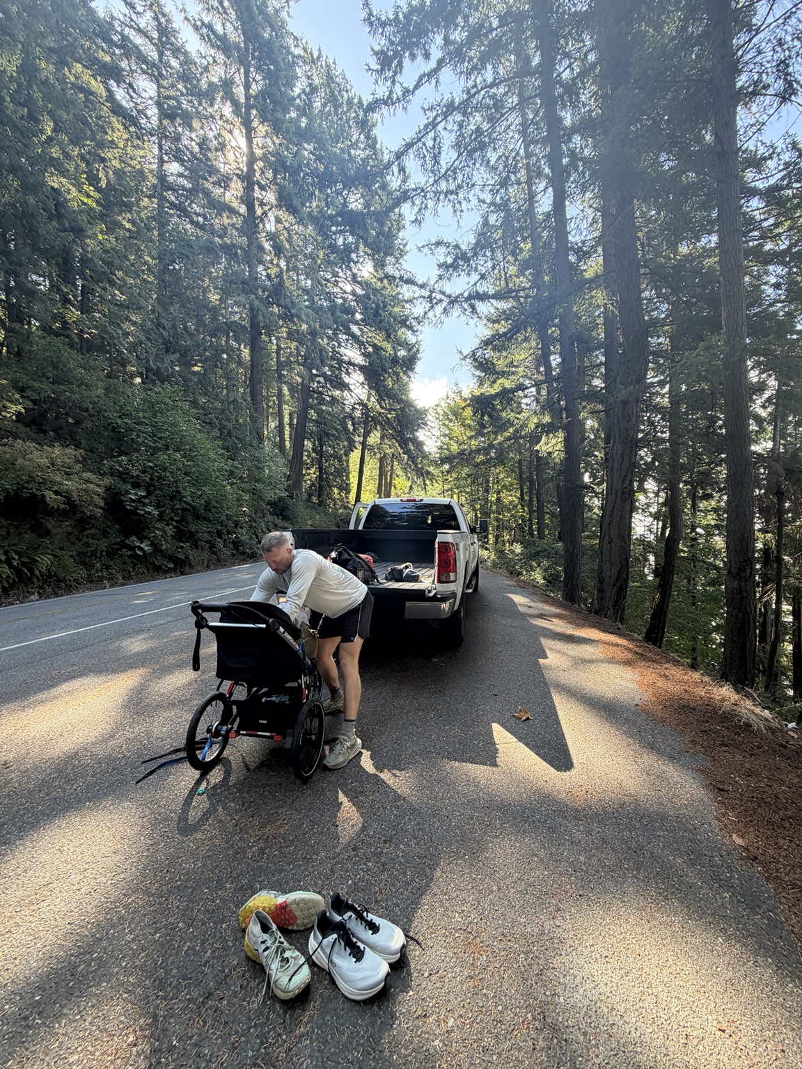Matthew changing shoes beside his running cart and support truck on a forest road