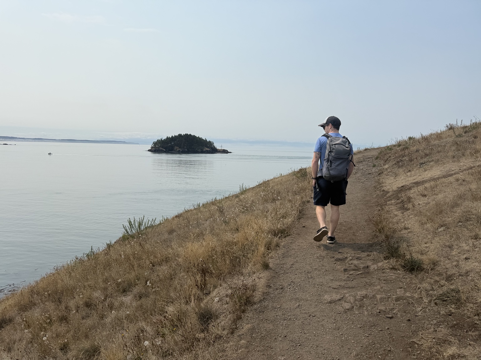 A friend walking a coastal trail above calm water near Deception Pass