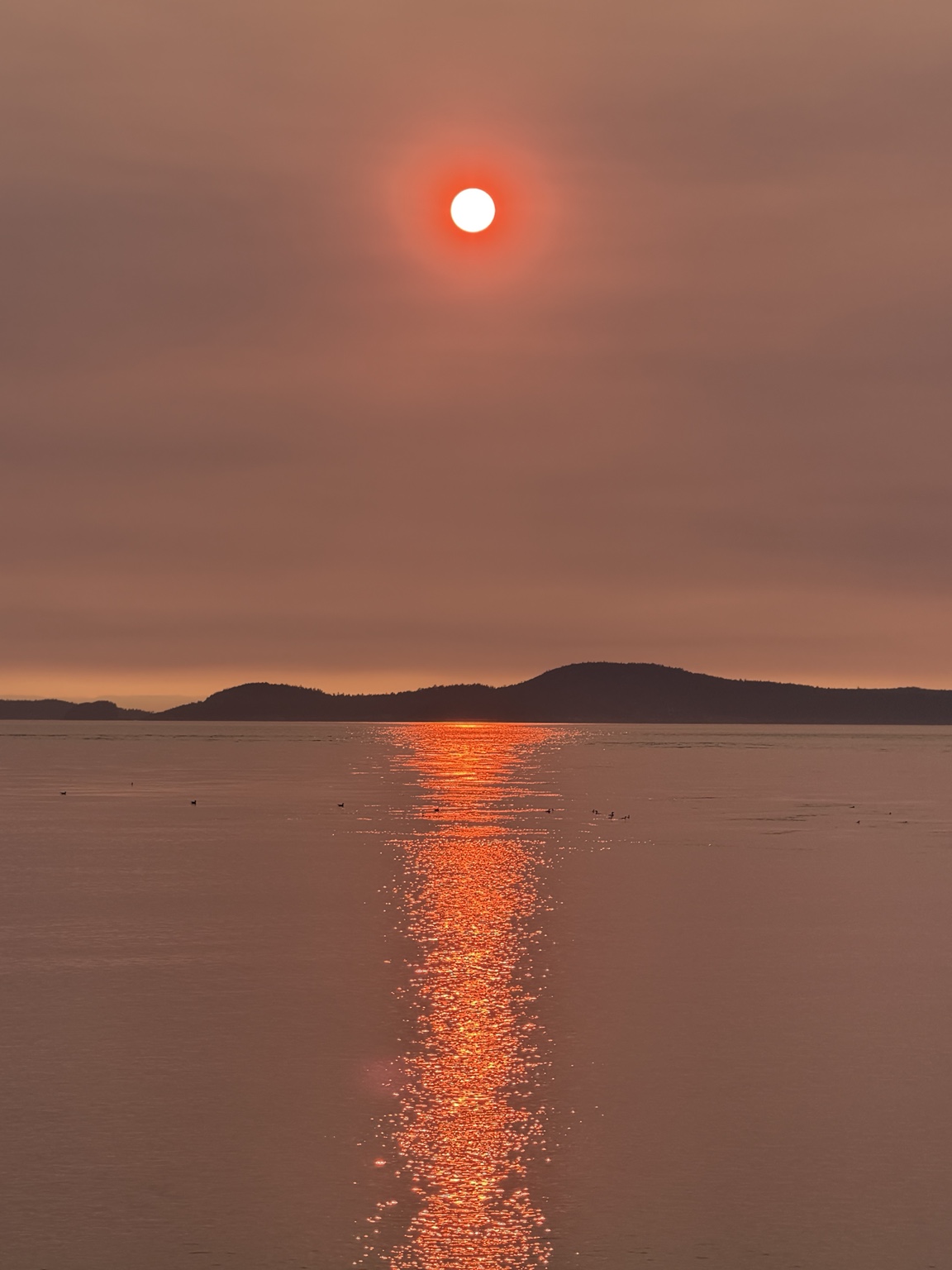 A glowing red sun setting over the water and distant islands