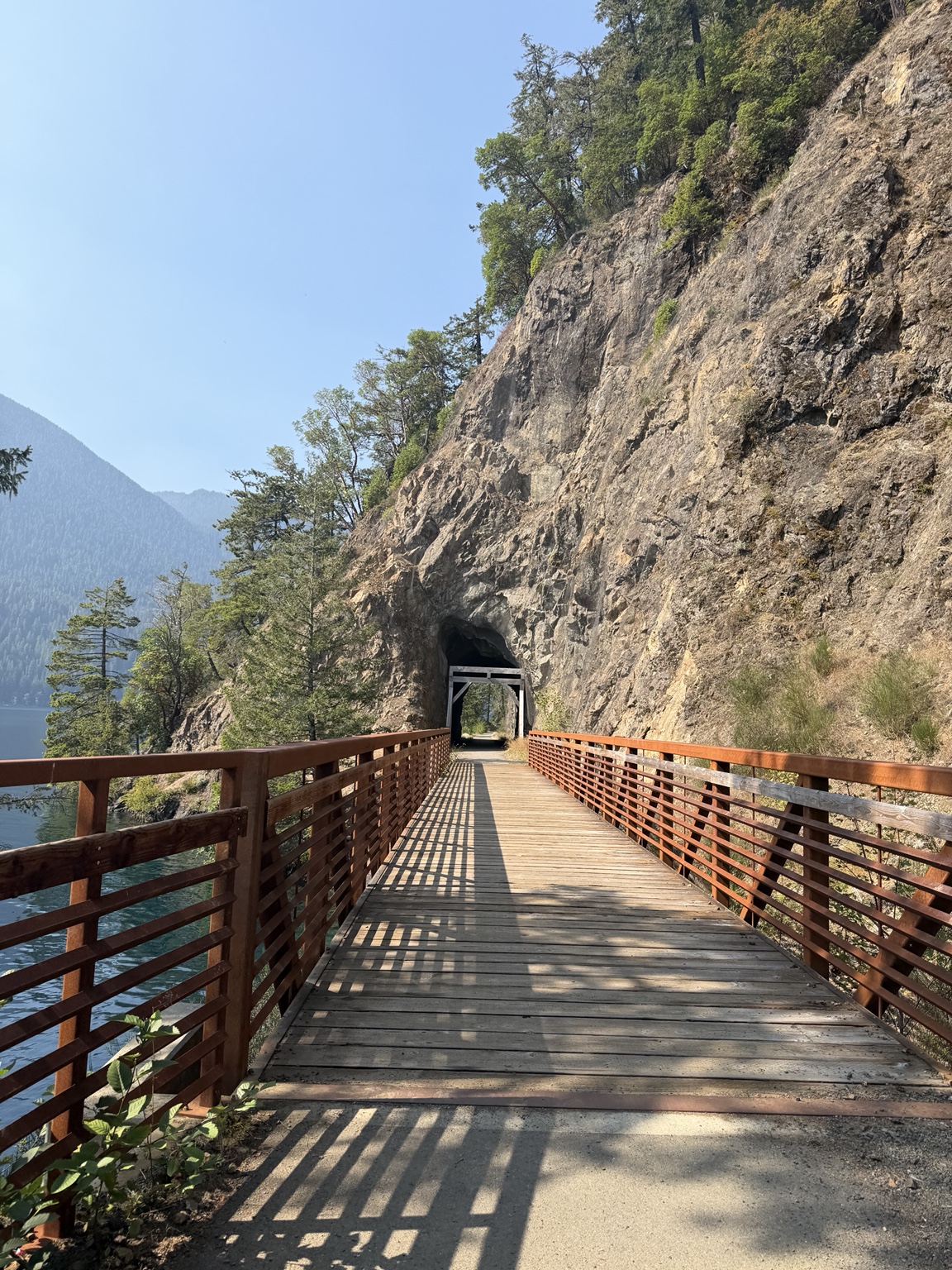 A wooden bridge leading toward a tunnel in the cliffs above Lake Crescent