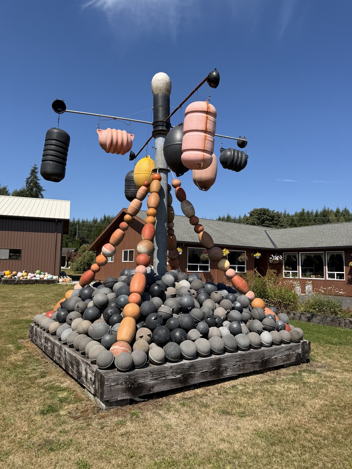 A tall human-shaped sculpture assembled from black, gray, orange, and pink fishing floats