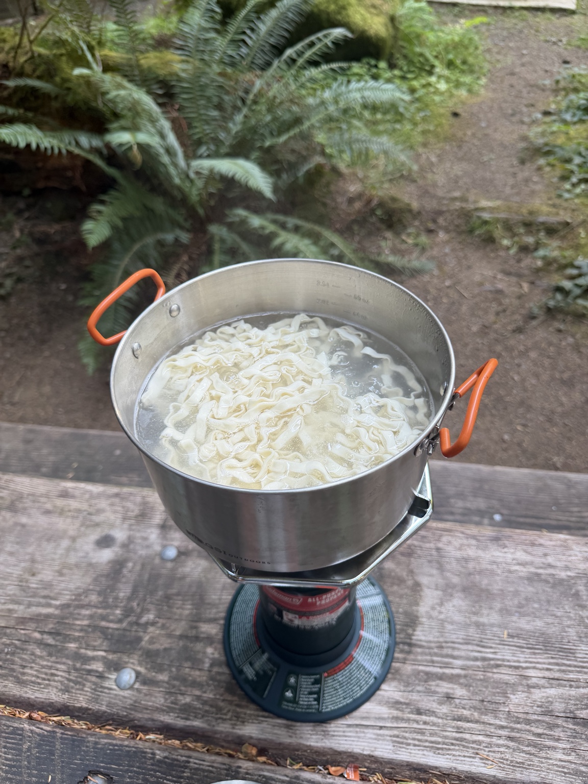 Noodles cooking on a compact camp stove at a picnic table