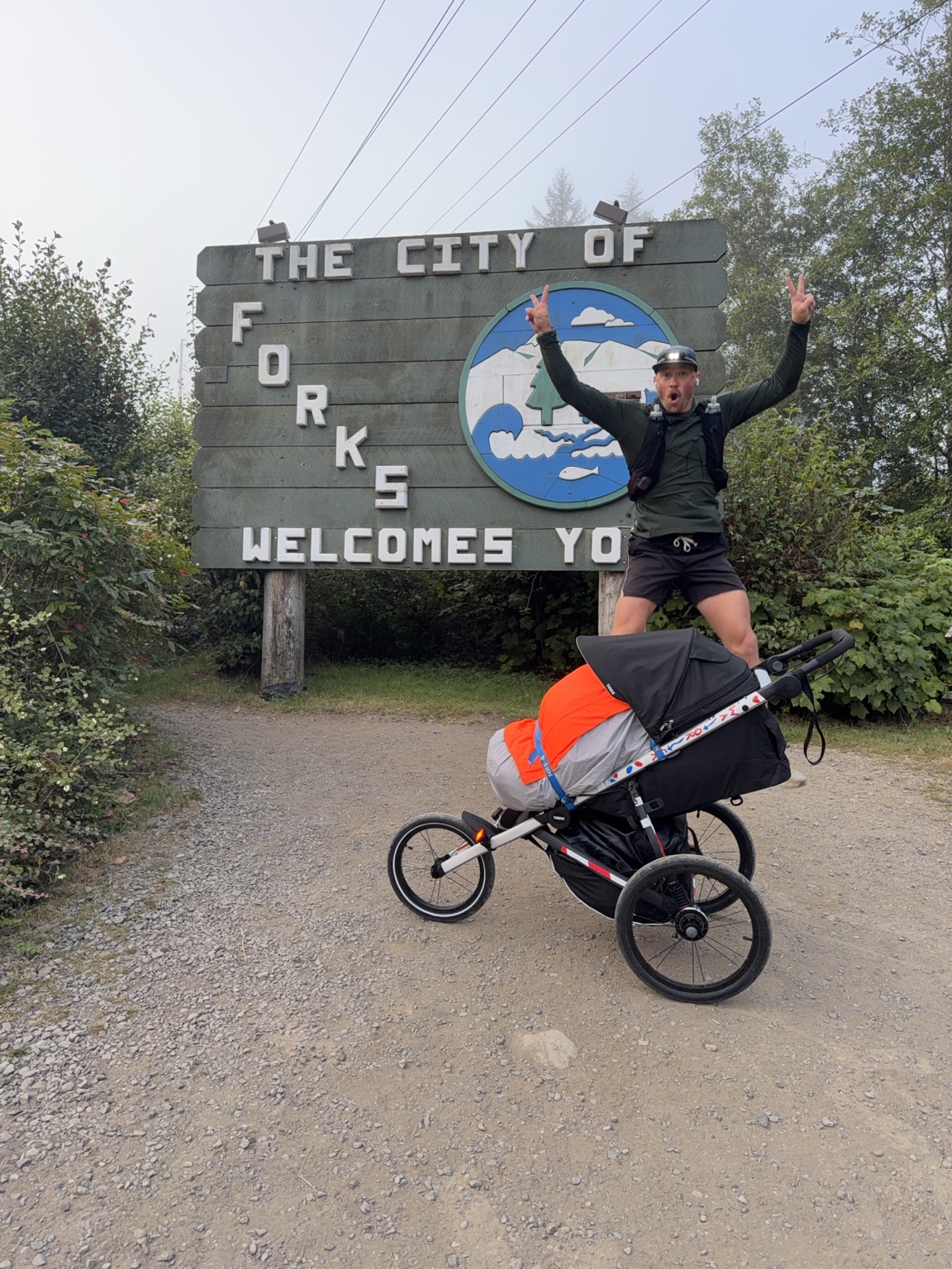 Matthew pushing his loaded running stroller past the City of Forks welcome sign