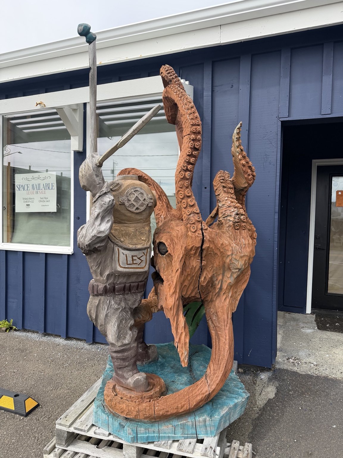A carved wooden deep-sea diver facing a giant octopus in a coastal town
