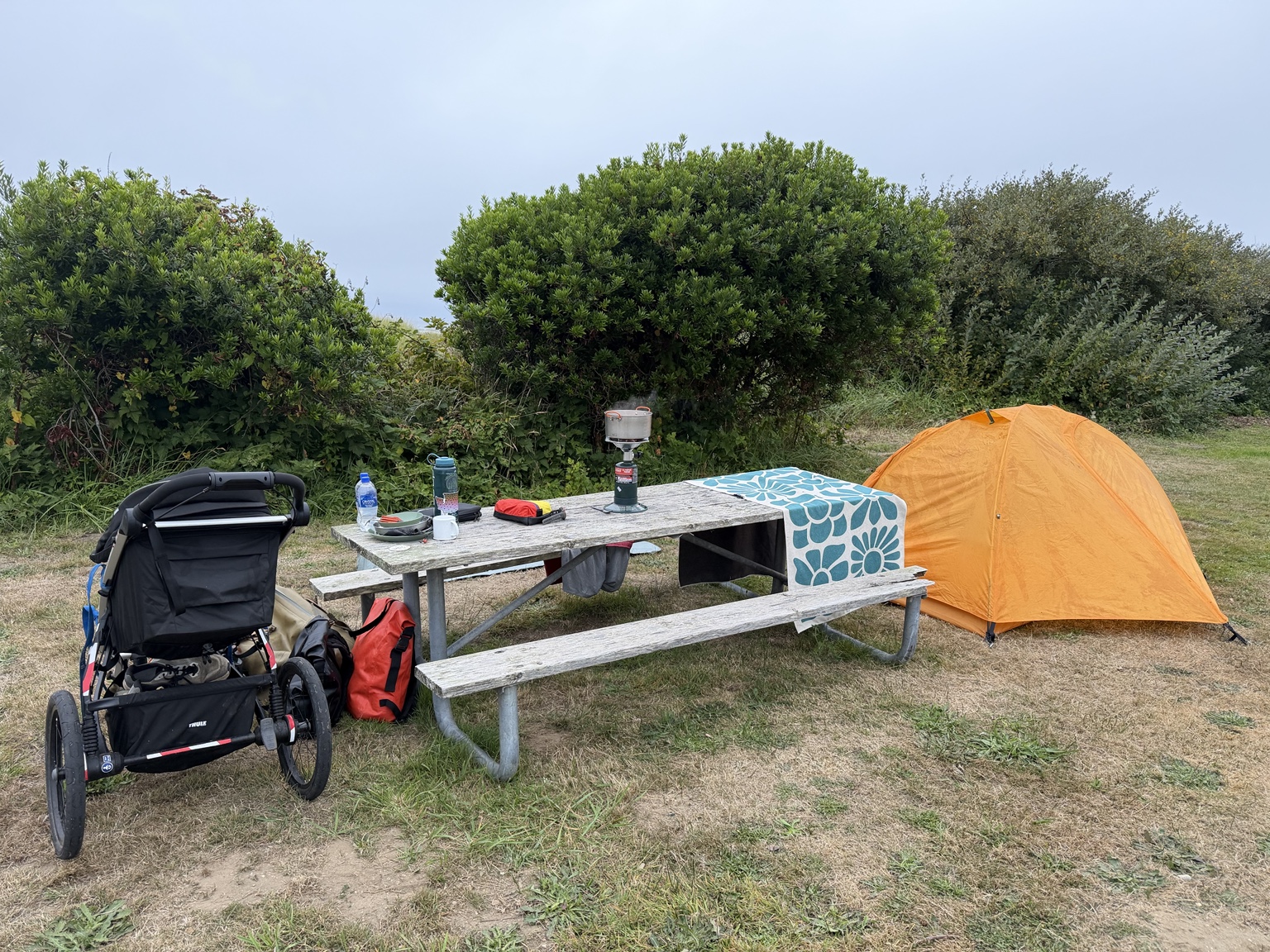 Matthew’s orange tent and loaded running stroller beside a picnic table at a coastal campsite