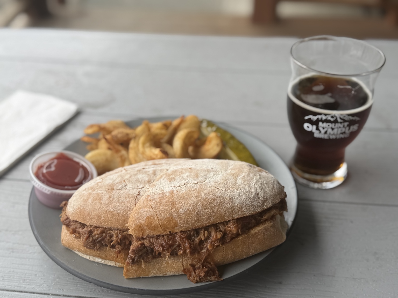 A pulled pork sandwich, fries, and a dark beer at Mount Olympus Brewing