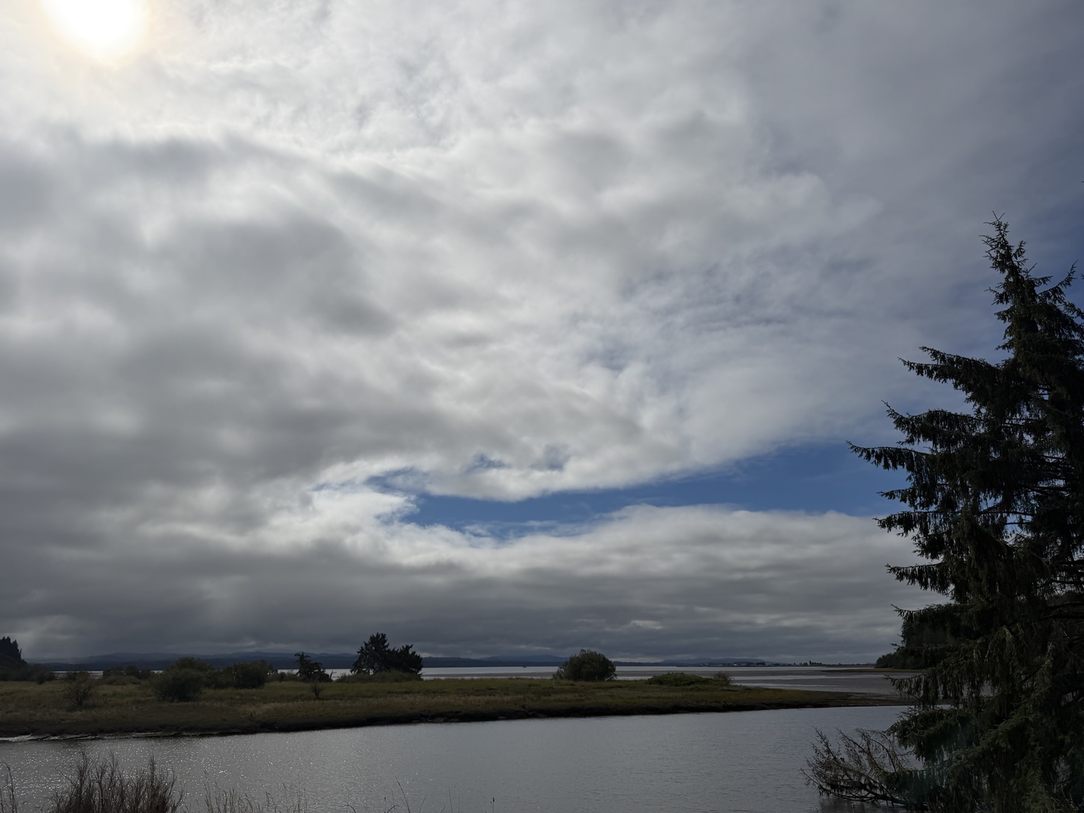 Sunlight breaking through clouds above a broad coastal estuary