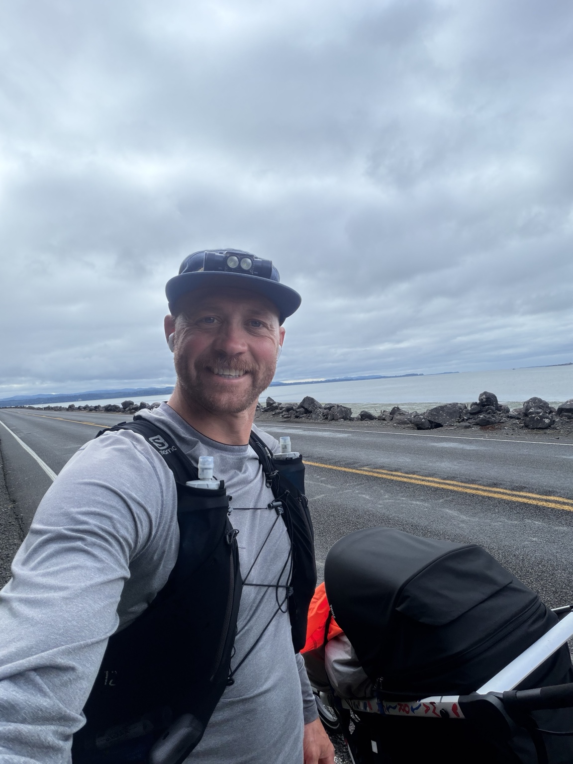 Matthew smiling beside his running stroller on the road along Willapa Bay