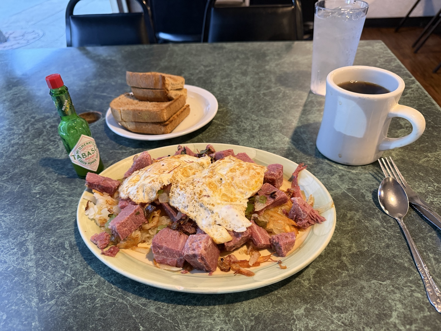 A hearty breakfast of corned beef hash, eggs, toast, coffee, and hot sauce