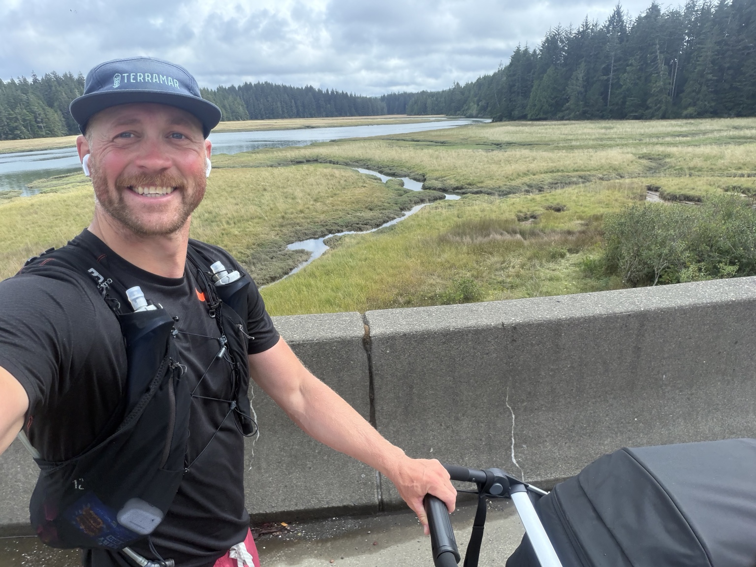 Matthew smiling beside his running stroller with a coastal estuary behind him