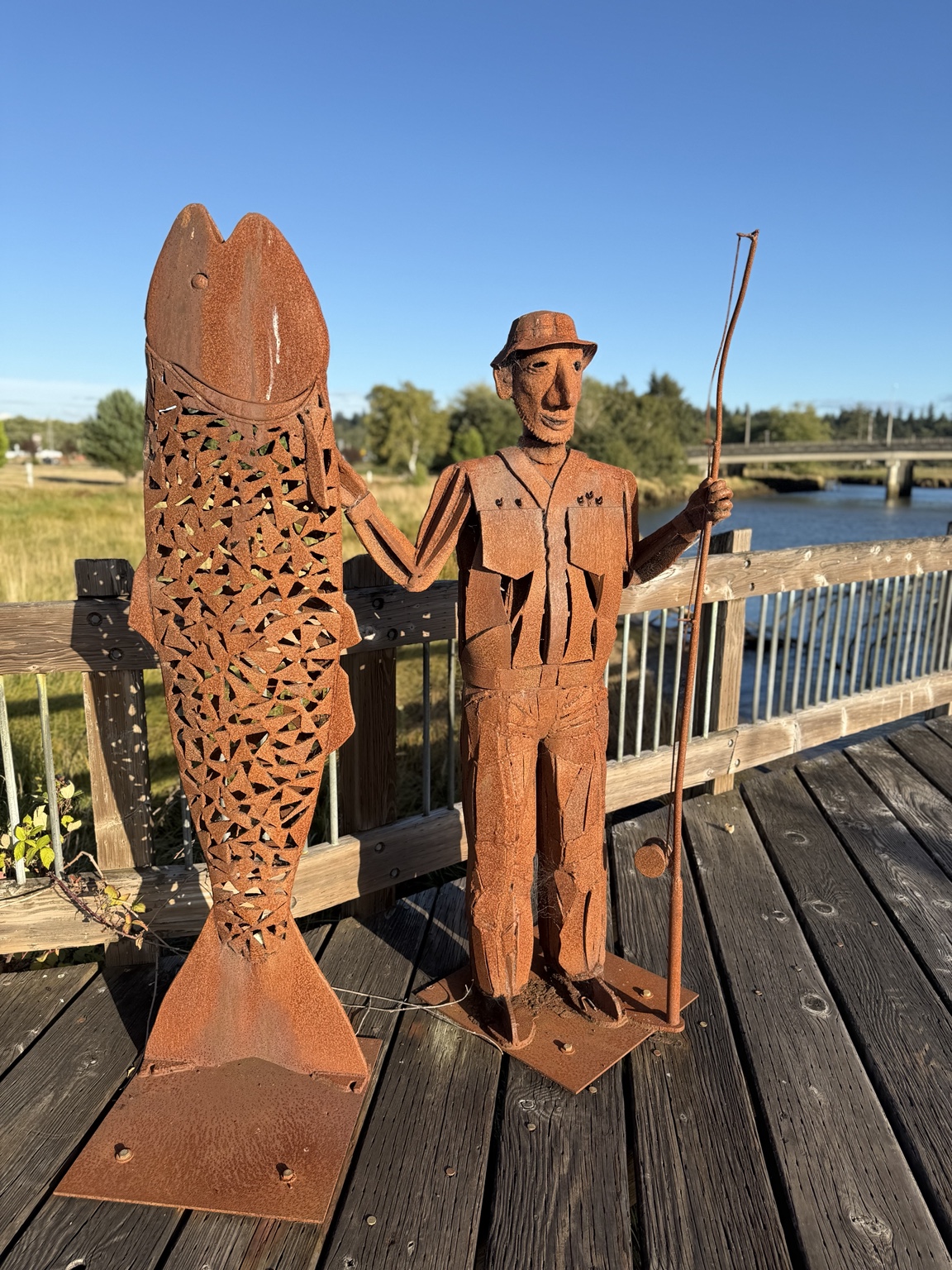 Rust-colored metal sculptures of a fisherman and fish beside the waterfront