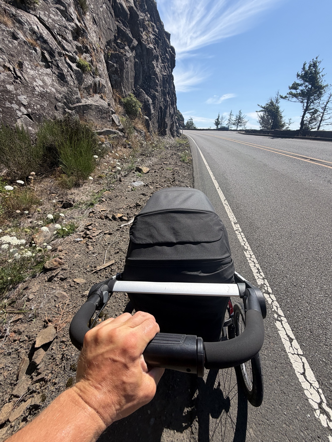 Matthew pushing his running stroller along a narrow highway shoulder beside a rocky cliff