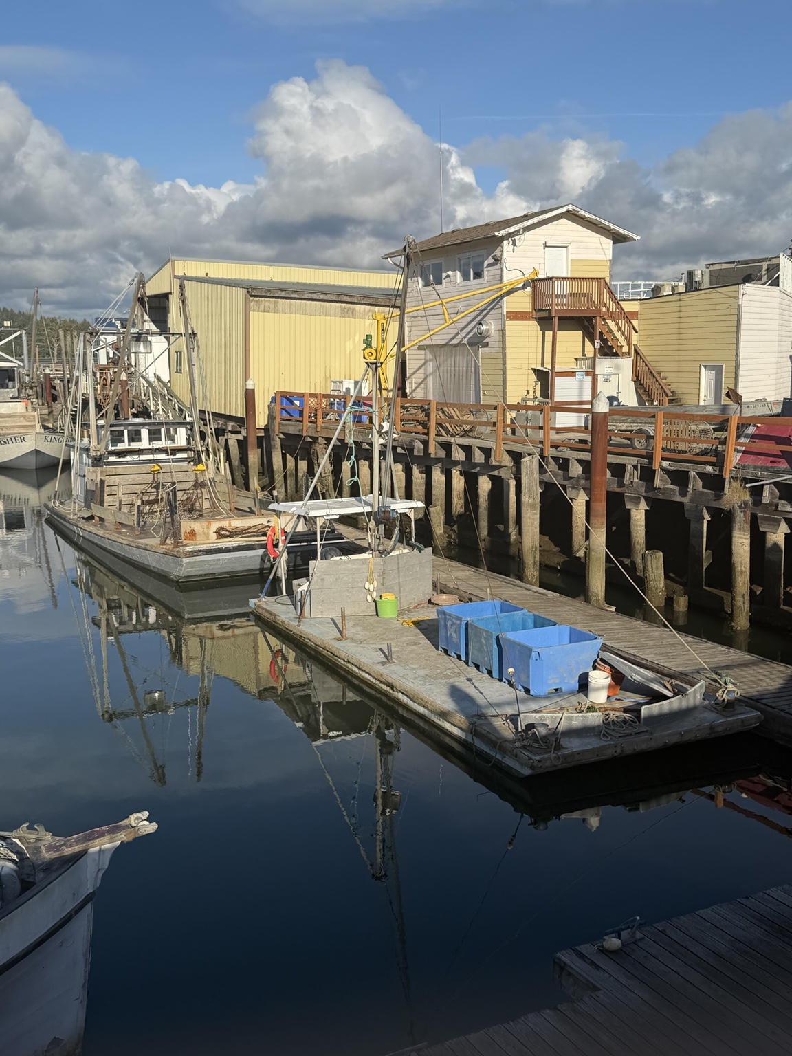 Fishing boats and working docks reflected in calm water beneath a bright coastal sky