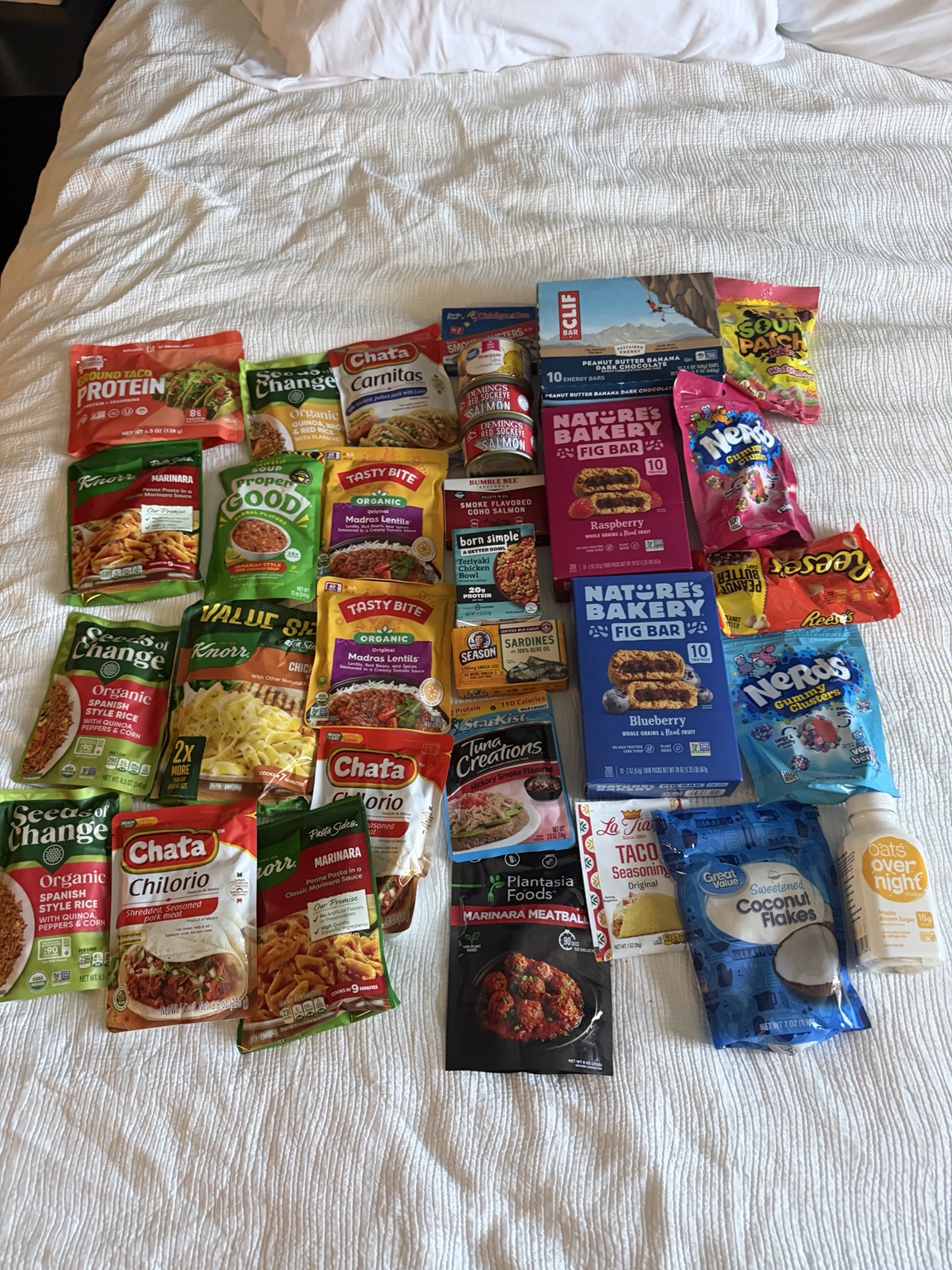 A fresh collection of trail meals, protein, snacks, and candy spread across a hotel bed