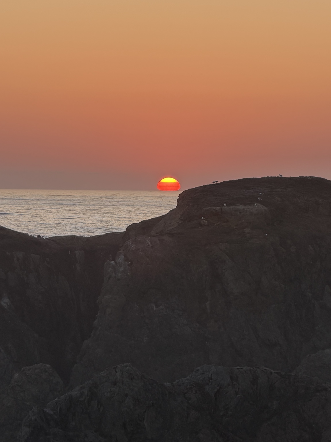 A bright orange sunset sinking into the Pacific beyond rocky cliffs near Bandon, Oregon
