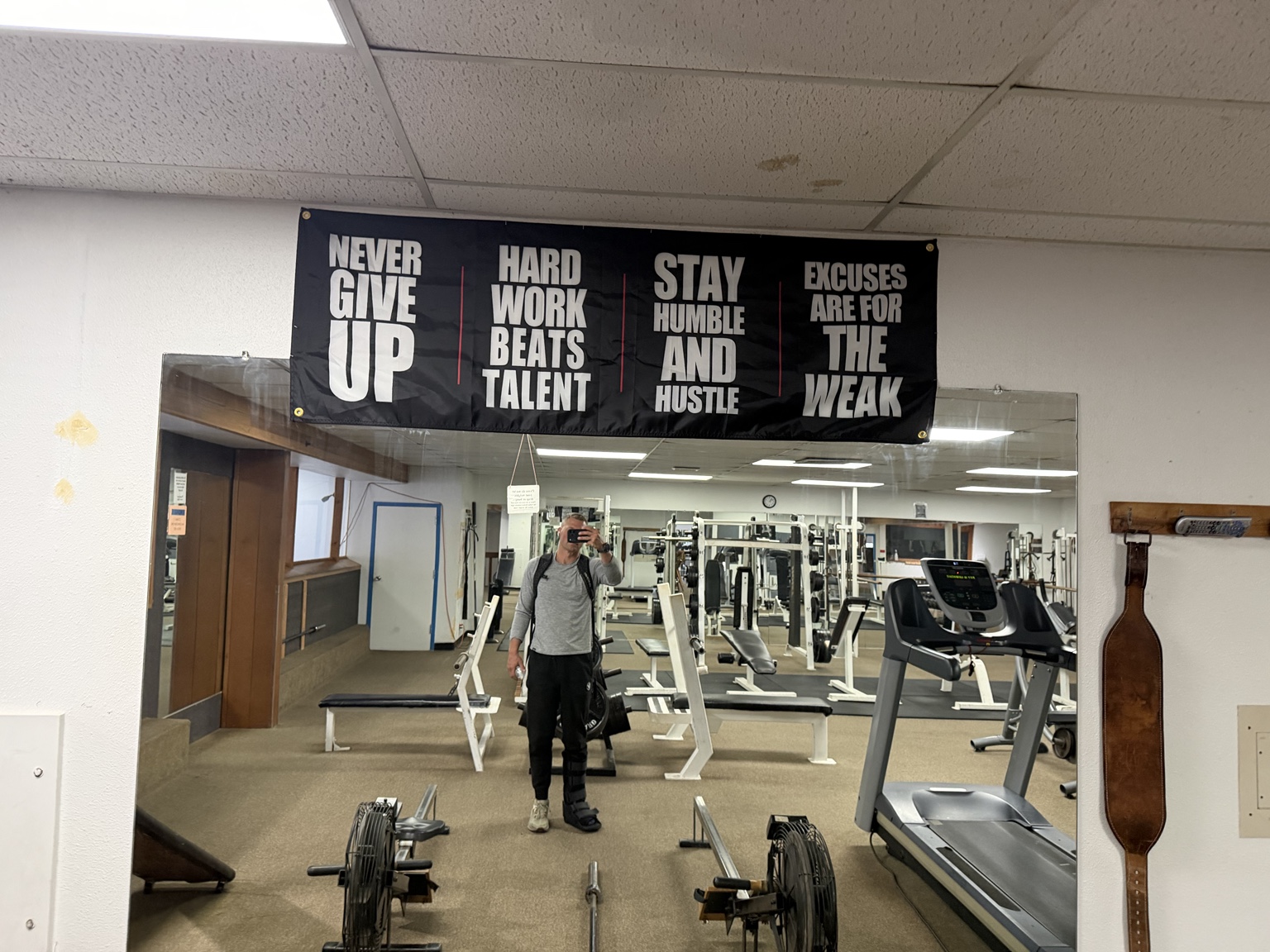 Matthew wearing a walking boot in the gym beneath a Never Give Up banner