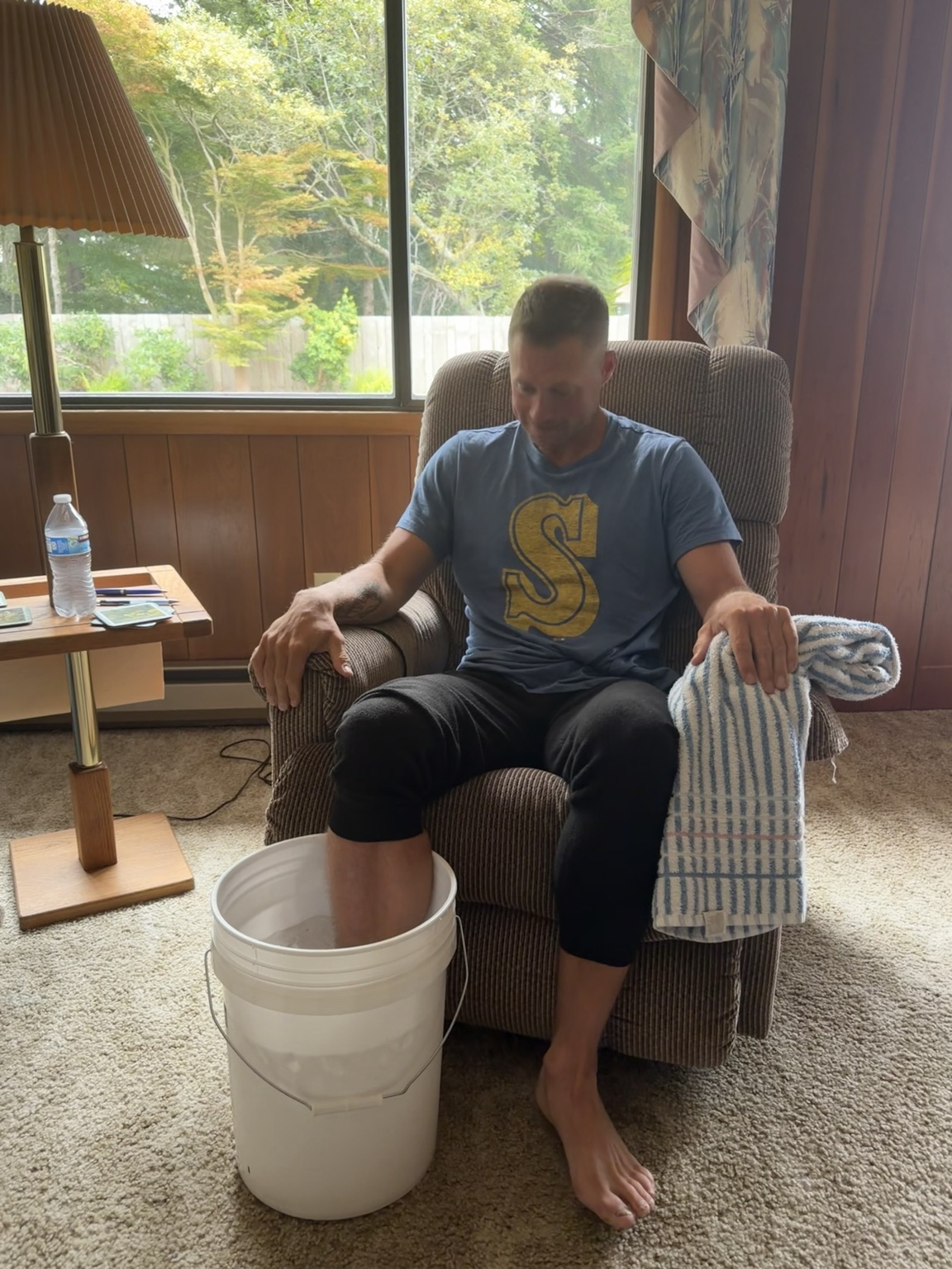 Matthew soaking his injured ankle in an ice bucket while resting at the family home