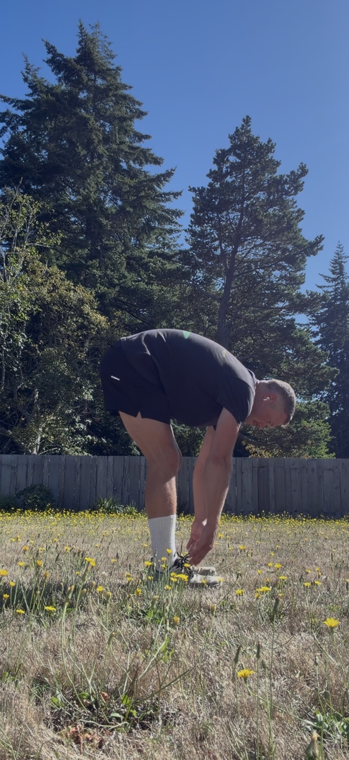 Matthew bending forward to stretch carefully in the yard during ankle recovery